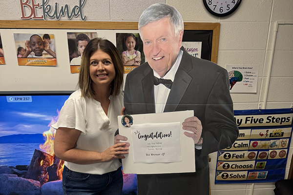 A woman poses with a cardboard cutout of a man in a suit holding a sign that say congratulations.